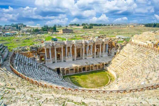 Wide view of Hierapolis theater beside the bright blue Pamukkale terraces.