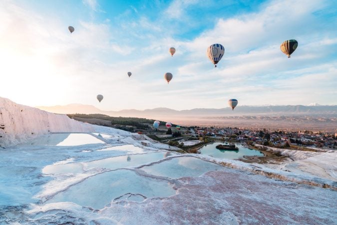 Hot air balloons flying over Pamukkale’s terraces in early morning.