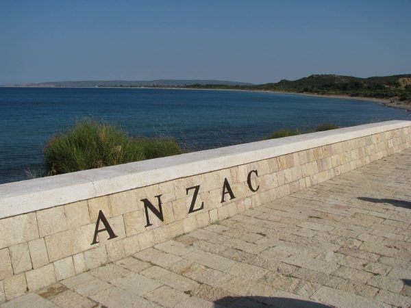 Seafront stone wall engraved with ANZAC beside calm water at Anzac Cove, Gallipoli