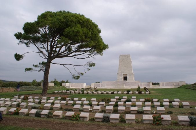 Single tree and distant memorial rising above rows of graves in Gallipoli war cemetery