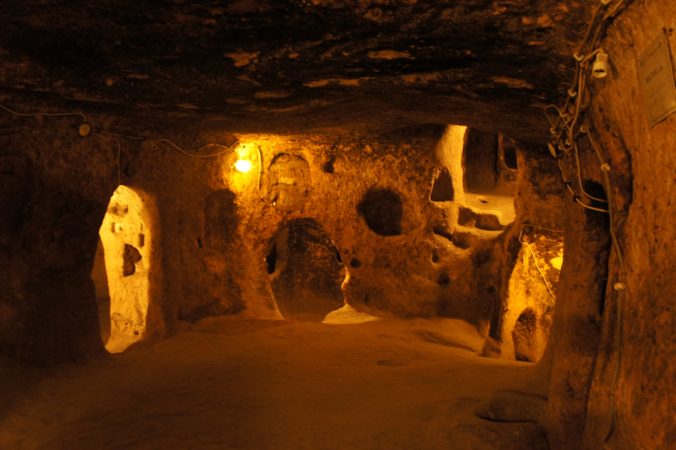 Rock-cut tunnels and connected chambers with warm lighting inside Kaymakli Underground City, Turkey.