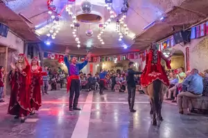 Un conjunto completo de bailarines folclóricos actuando juntos en el escenario del espectáculo de noche turca de Capadocia, parte de un paquete de tour de visitas locales. La colorida actuación grupal muestra la diversidad de las danzas regionales de Anatolia y las tradiciones culturales.