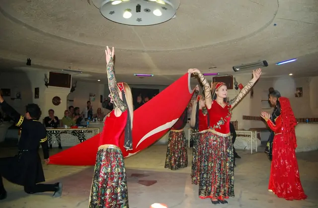 Una artista femenina con un vistoso traje rojo levanta los brazos con gracia durante la experiencia de excursión de un día del espectáculo de noche turca de Capadocia. Su expresiva pose y el traje tradicional encarnan la pasión y la elegancia de la danza folclórica de Anatolia en esta celebrada cena