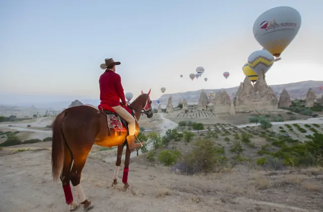 Donna con casco su un cavallo marrone con vista sui camini delle fate della Cappadocia