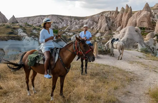 Donna a cavallo all'alba in Cappadocia con mongolfiere nel cielo
