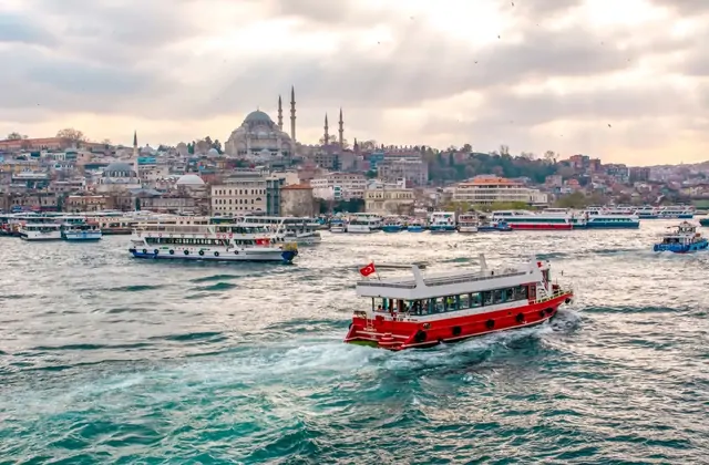 Una barca da crociera rossa attraversa il Bosforo con lo skyline di Istanbul sullo sfondo, creando una scena di viaggio colorata e iconica lungo la via d'acqua più famosa della Turchia.