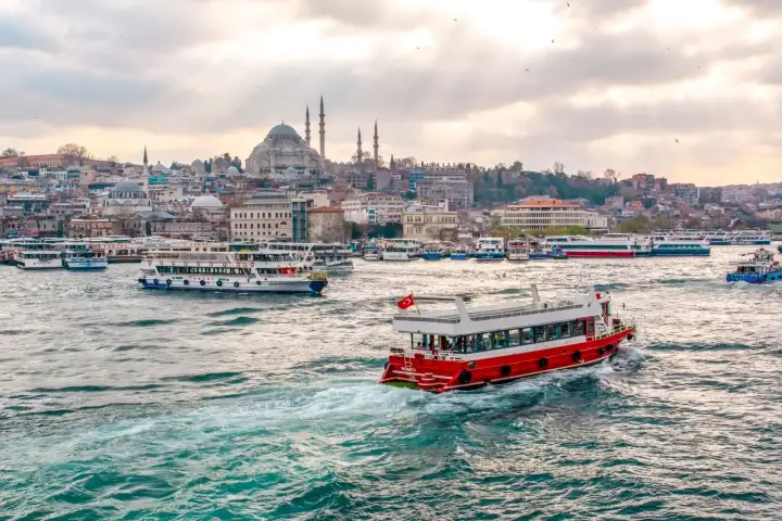 Una barca da crociera rossa attraversa il Bosforo con lo skyline di Istanbul sullo sfondo, creando una scena di viaggio colorata e iconica lungo la via d'acqua più famosa della Turchia.