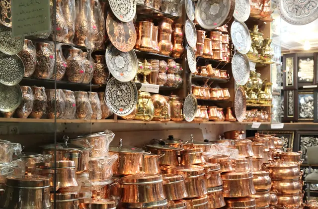 Gli scaffali dal pavimento al soffitto in un negozio del bazar del rame di Gaziantep sono affollati da file di pentole di rame impilate e caffettiere turche, mentre la parete di fondo espone piatti decorativi incisi, vassoi ornati e un samovar in ottone.
