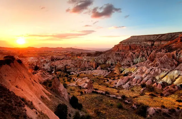 Vista panorámica a lo largo del Güllüdere (Valle de la Rosa) hacia Çavuşin en Capadocia, con vegetación y entradas a cuevas en la ruta de senderismo del Yellow Tour.