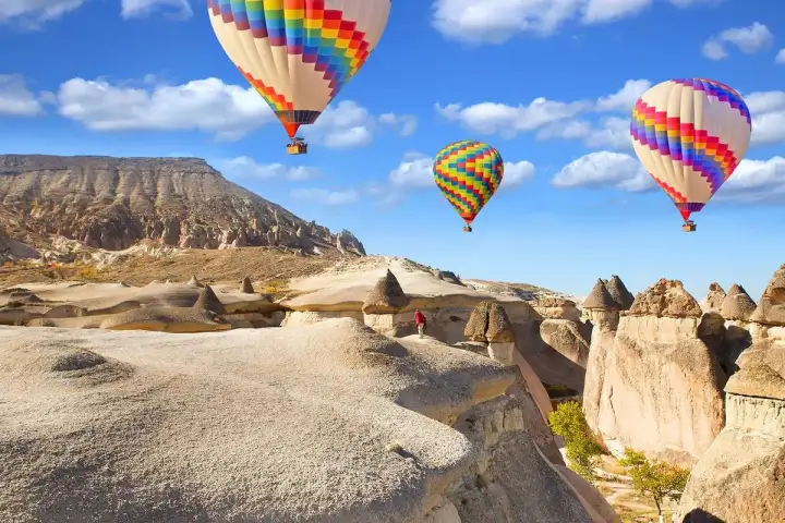 Hot air balloons pass over Cappadocia's iconic mushroom-shaped rock formations under a vivid blue sky, Turkey, offering a dramatic contrast between the earthly spires and the floating crafts.