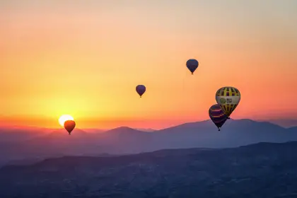 Before sunrise, hot air balloons rise over the Göreme valley of Cappadocia, Turkey, their glowing envelopes cutting through the deep blue pre-dawn sky above the ancient cave town.