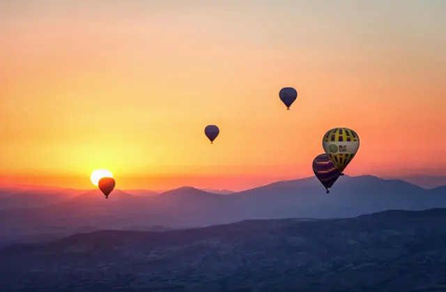 Before sunrise, hot air balloons rise over the Göreme valley of Cappadocia, Turkey, their glowing envelopes cutting through the deep blue pre-dawn sky above the ancient cave town.