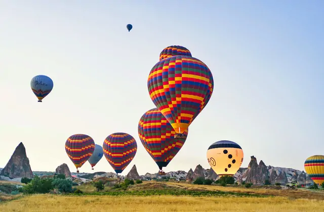 Bold checkered hot air balloons in red, blue, and yellow fly over the fairy chimneys of Cappadocia, Turkey, the geometric patterns contrasting sharply with the organic shapes of the volcanic rock below.