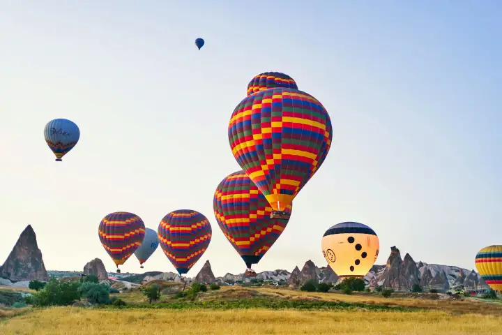 Audaci mongolfiere a scacchi in rosso, blu e giallo volano sui camini di fate della Cappadocia, Turchia, i motivi geometrici che contrastano nettamente con le forme organiche della roccia vulcanica sottostante.