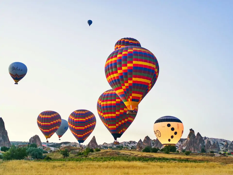 Audaci mongolfiere a scacchi rosse, blu e gialle volano sopra i camini delle fate della Cappadocia, Turchia, creando un netto contrasto tra i motivi geometrici e le forme organiche della roccia vulcanica sottostante.