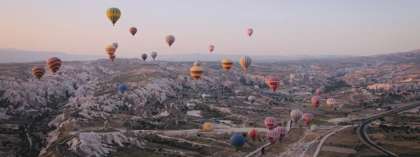Vista dall'alto all'alba, la piana della Cappadocia in Turchia è disseminata di decine di mongolfiere a varie altitudini, formando uno spettacolare spettacolo aereo sulle valli erose.