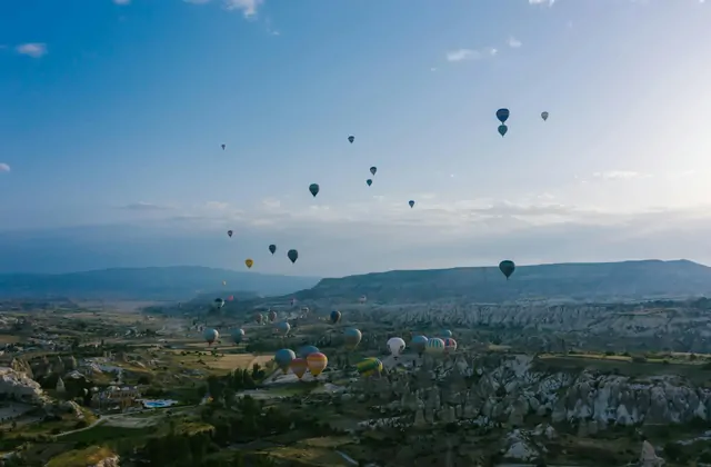 Una vista aerea sulla Cappadocia, Turchia, mostra una strada tortuosa che taglia attraverso valli di roccia erosa mentre le mongolfiere si librano a diverse altezze nel cielo circostante.
