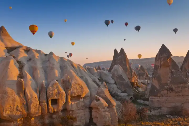 La luce dell'ora d'oro avvolge i camini di fate della Cappadocia, Turchia, in un caldo ambra mentre le mongolfiere derivano tra le alte guglie vulcaniche, proiettando lunghe ombre sul fondo della valle.