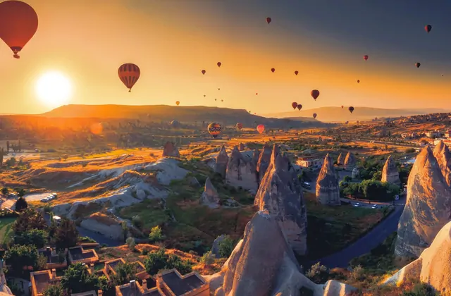 La luce dorata dell'alba spazza i camini di fate e i tetti di un paese nella valle della Cappadocia, Turchia, trasformando il paesaggio vulcanico in uno scenario di straordinario calore cromatico.