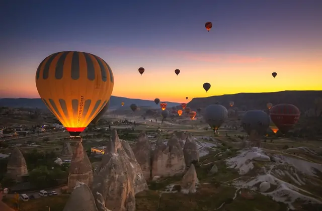 All'alba sulla Cappadocia, Turchia, i bruciatori delle mongolfiere in ascesa brillano di arancione contro il cielo scuro, proiettando luce calda sull'antico paesaggio dei camini di fate sottostante.