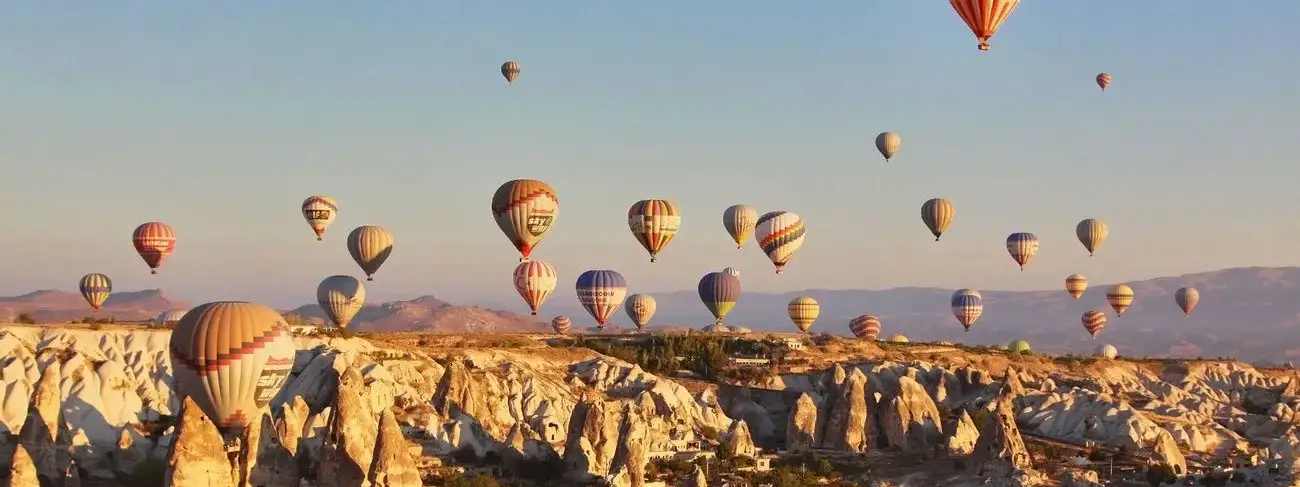 Altas chimeneas de hadas se elevan desde la meseta de Capadocia, Turquía, mientras el cielo matinal encima está lleno de vida con decenas de globos aerostáticos a diferentes altitudes que derivan en el aire tranquilo.