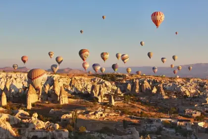 Tall fairy chimneys rise from the Cappadocian plateau, Turkey, while the morning sky above is alive with dozens of hot air balloons at various altitudes drifting in the still air.