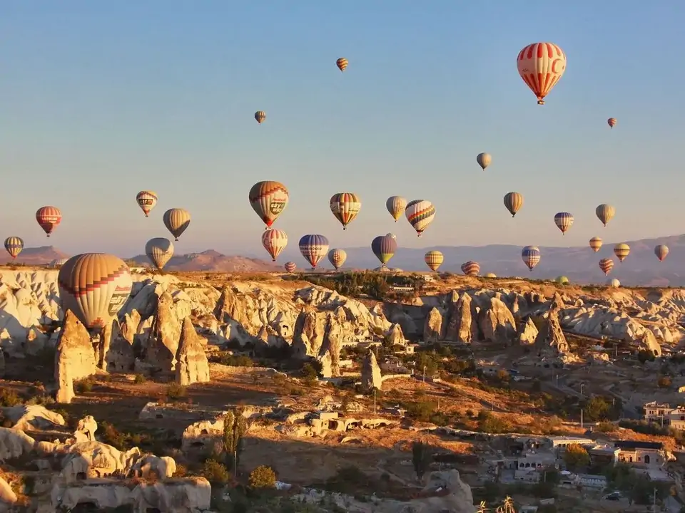 Alti camini delle fate si innalzano dall’altopiano della Cappadocia, Turchia, mentre il cielo del mattino si anima con decine di mongolfiere a diverse altitudini che fluttuano nell’aria calma.