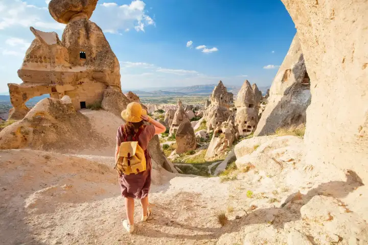 A female traveler stands at a panoramic viewpoint overlooking a cave city carved into the cliffs of Cappadocia, Turkey, taking in the vast scale of the ancient rock-hewn settlement.