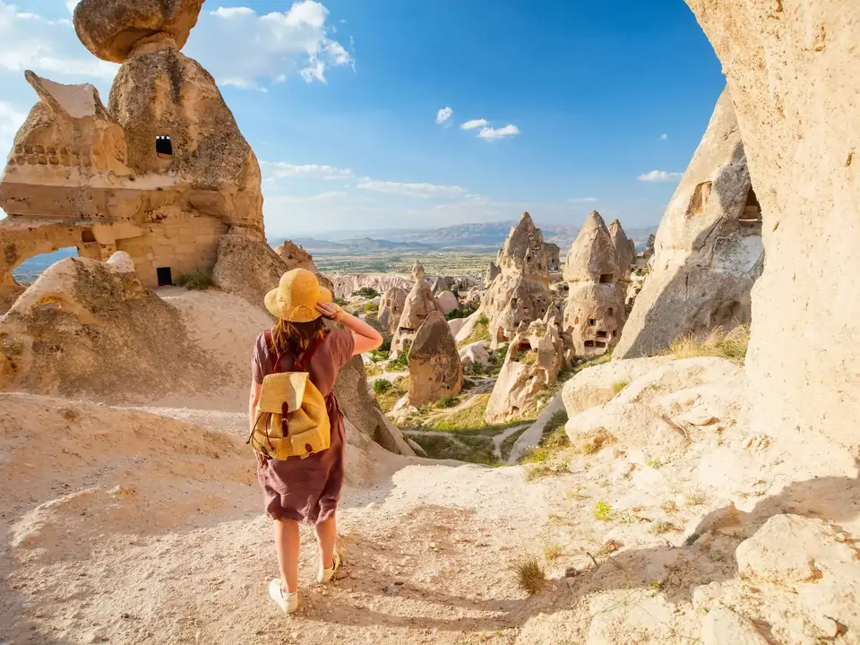 Una viaggiatrice osserva da un punto panoramico una città rupestre scavata nelle scogliere della Cappadocia, in Turchia, cogliendo la grande scala dell’antico insediamento scavato nella roccia.