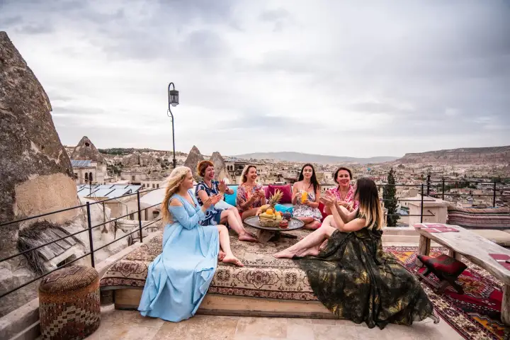 Un gruppo di amici condivide una colazione turca tradizionale su una terrazza sul tetto a Göreme, Cappadocia, Turchia, con le case rupestri e i camini del paese che si estendono sotto di loro.