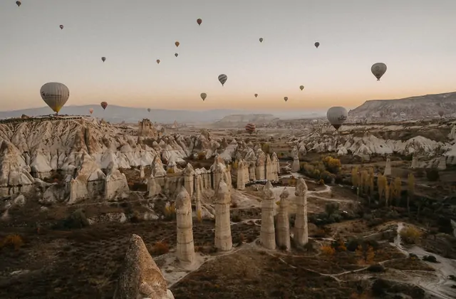 Al crepuscolo nella Valle dell'Amore, Cappadocia, Turchia, i pilastri di pietra svaniscono nell'ombra profonda mentre le ultime mongolfiere della giornata galleggiano sopra di essi nel cielo violetto e indaco.
