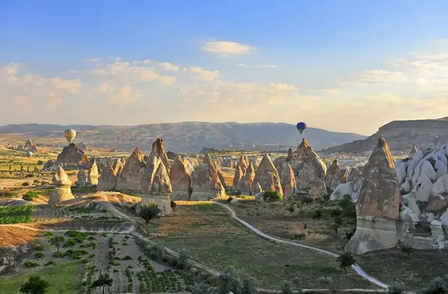 El minarete de una mezquita se eleva junto a casas talladas en cuevas en un panorama de un pueblo de Capadocia, Turquía, mientras un grupo de globos aerostáticos flota sobre el paisaje volcánico.