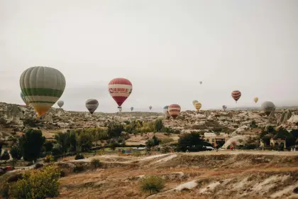 Under a soft overcast sky, a balloon tour floats above the broad Cappadocia plateau, Turkey, the diffused light creating an even, atmospheric view of the eroded valleys and rock formations below.