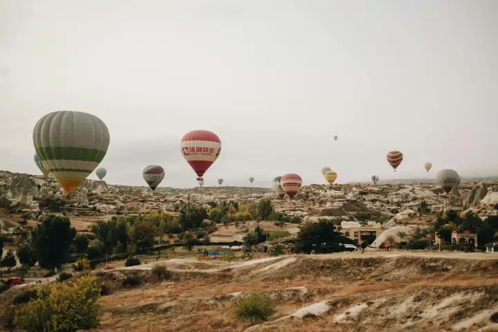 Sotto un morbido cielo coperto, un tour in mongolfiera galleggia sull'ampio altopiano della Cappadocia, Turchia, la luce diffusa che crea una vista uniforme e atmosferica delle valli erose e delle formazioni rocciose sottostanti.