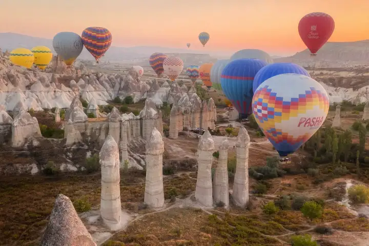 Las distintivas chimeneas de hadas de cabezas múltiples de Pasabağ (Valle de los Monjes) en Capadocia, Turquía, se elevan altas al amanecer mientras los globos ascienden en el cielo rosado y luminoso.