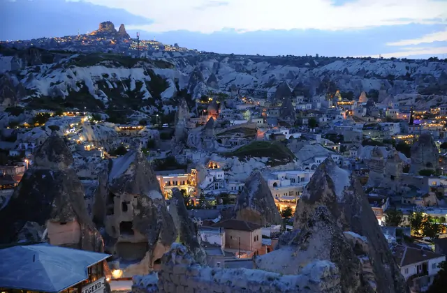 Un panorama notturno dell'ora blu di Göreme, Cappadocia, Turchia, cattura il borgo rupestre che brilla di luci calde annidato tra scure formazioni di roccia vulcanica sotto un profondo cielo al crepuscolo.