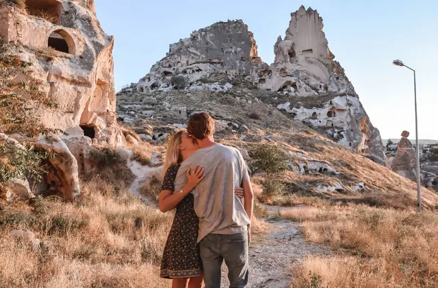 Una pareja comparte un abrazo romántico cerca de las casas de roca cueva de Capadocia, Turquía, las antiguas fachadas de piedra tallada proporcionando un íntimo telón de fondo a su momento juntos.