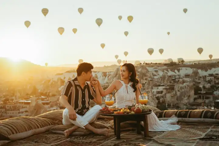 Una coppia condivide un'intima colazione sul tetto all'alba in Cappadocia, Turchia, la luce calda che illumina la tavola apparecchiata con formaggi turchi, olive e tè mentre la valle brilla in basso.