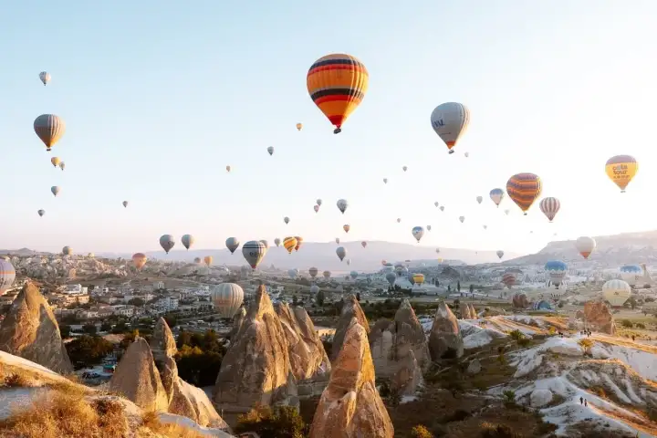 Al crepuscolo sul tetto di un hotel grotta della Cappadocia, una coppia guarda le ultime mongolfiere della giornata passare, il cielo violetto dietro di loro che sfuma sulle sagome del valle roccioso.