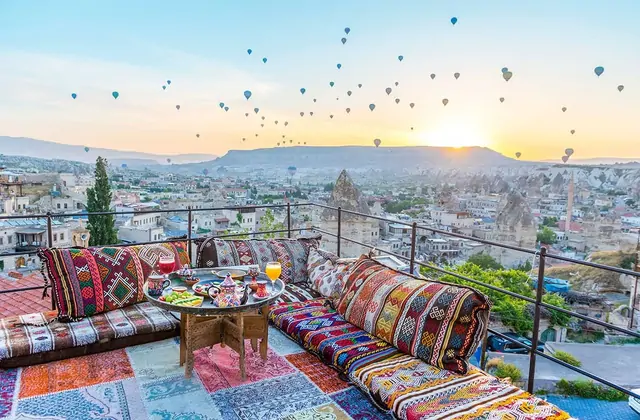 A beautifully set breakfast corner on a Cappadocian rooftop terrace overlooks the sunrise balloon spectacle, Turkey, where dozens of colorful balloons fill the sky above the cave-carved landscape.