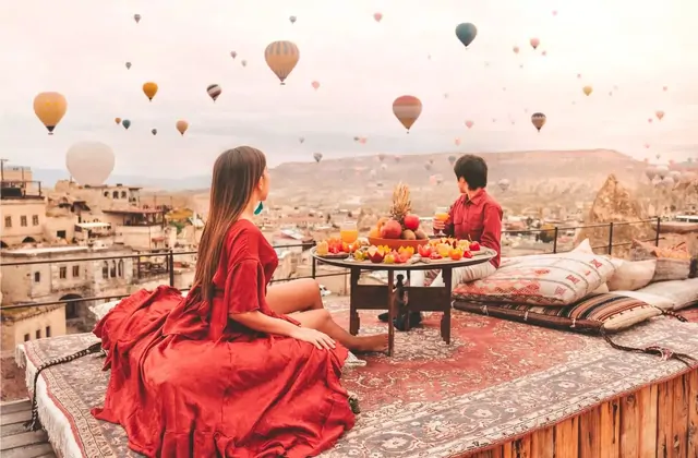 Un desayuno turco tradicional está dispuesto en una terraza de la azotea en Capadocia, Turquía, enmarcando un cielo de amanecer donde los globos aerostáticos se elevan sobre el antiguo pueblo de piedra abajo.
