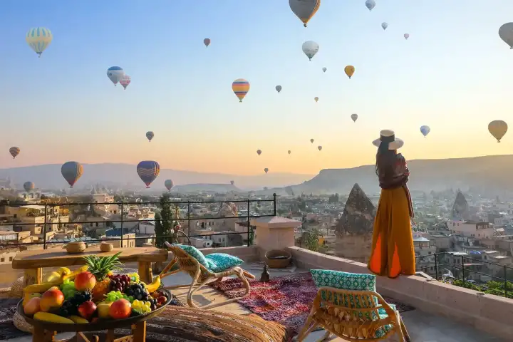In piedi a un belvedere sul tetto in Cappadocia, Turchia, una donna guarda il cielo pre-alba riempirsi dei luminosi involucri di decine di mongolfiere che iniziano la loro ascesa mattutina.