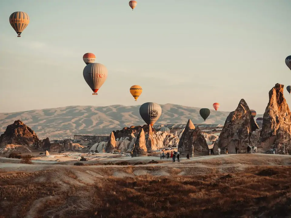Spettacolari guglie rocciose emergono dal paesaggio della Cappadocia, Turchia, mentre le mongolfiere si muovono tra le alte formazioni in una scena che unisce perfettamente meraviglia naturale e avventura aerea.
