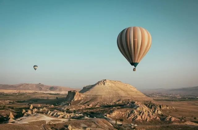 Una singola mongolfiera solitaria galleggia sopra il paesaggio a mesa dalla sommità piatta della Cappadocia, Turchia, la sua presenza solitaria che sottolinea la vasta scala dell'altopiano eroso che si estende fino all'orizzonte.