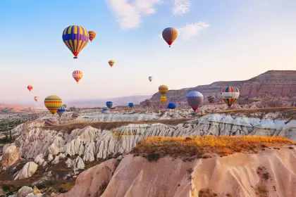 Mongolfiere con strisce arcobaleno e multicolori navigano sopra un paesaggio di creste vulcaniche bianche in Cappadocia, Turchia, il brillante spettro di colori vivido contro le pale formazioni di pietra.