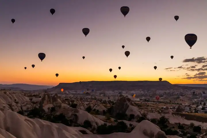 Al amanecer sobre Capadocia, Turquía, los globos aerostáticos aparecen como siluetas oscuras contra el ardiente horizonte naranja, sus formas suspendidas sobre el vasto panorama de valles erosionados.