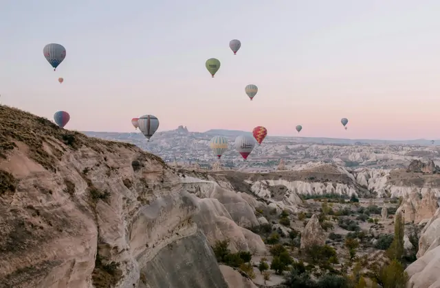Hot air balloons drift above the layered mountain horizon of Cappadocia at sunset, Turkey, the fading light creating bands of gold, orange, and purple across the volcanic skyline.