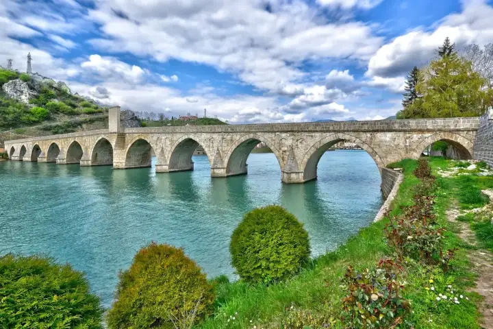 The ten-arched Artuklu Bridge at Diyarbakır spans the Tigris River, its black basalt piers rising from turquoise-tinted water that shimmers in the bright midday sun, framing a classic Mesopotamian holiday destination view.