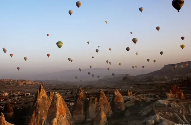 Al crepuscolo su una valle di camini di fate in Cappadocia, Turchia, l'ultimo volo in mongolfiera della giornata planea attraverso un cielo lavanda e indaco sopra le guglie di roccia che si fanno scure.