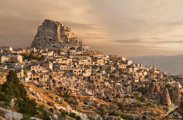 Uçhisar Castle, the highest point in Cappadocia, Turkey, commands a golden-hour panorama over the surrounding townscape of cave houses and rock-cut dwellings bathed in warm evening light.